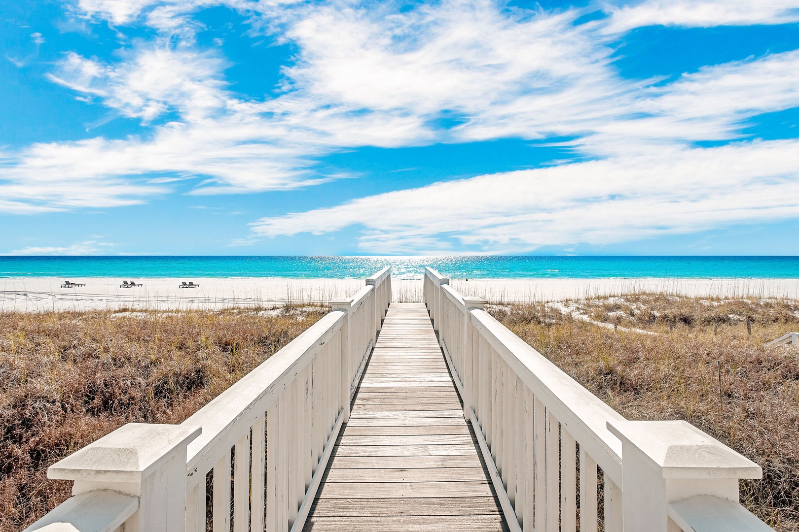 A wooden boardwalk leads through natural dunes to a pristine white-sand beach and sparkling turquoise waters, offering convenient access to the nearby shoreline and ocean.