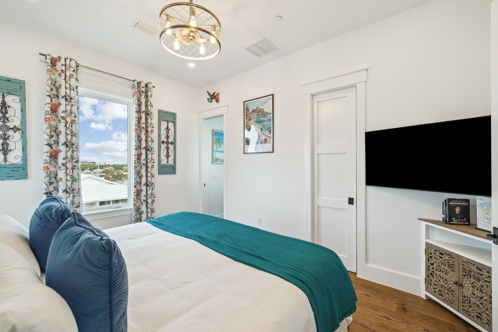 Unwind in this elegant bedroom featuring crisp white linens with turquoise accents, coastal artwork, and your own entertainment center for cozy evenings.