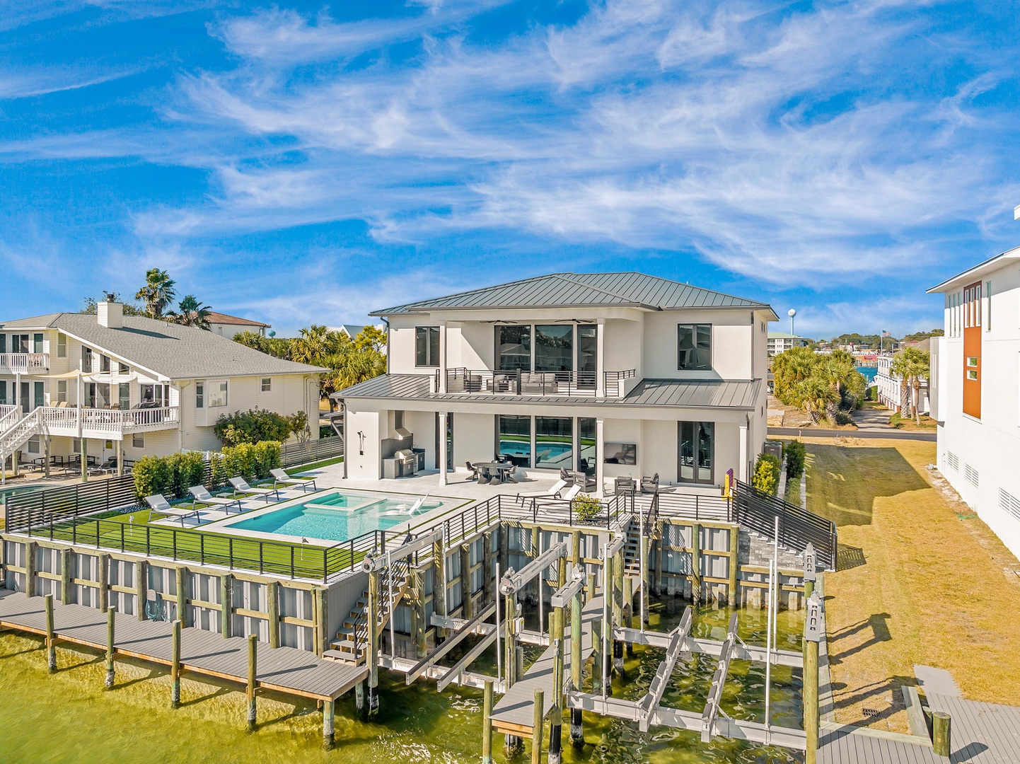 Modern waterfront property featuring a private pool and boat dock in a scenic coastal neighborhood with clear blue skies.