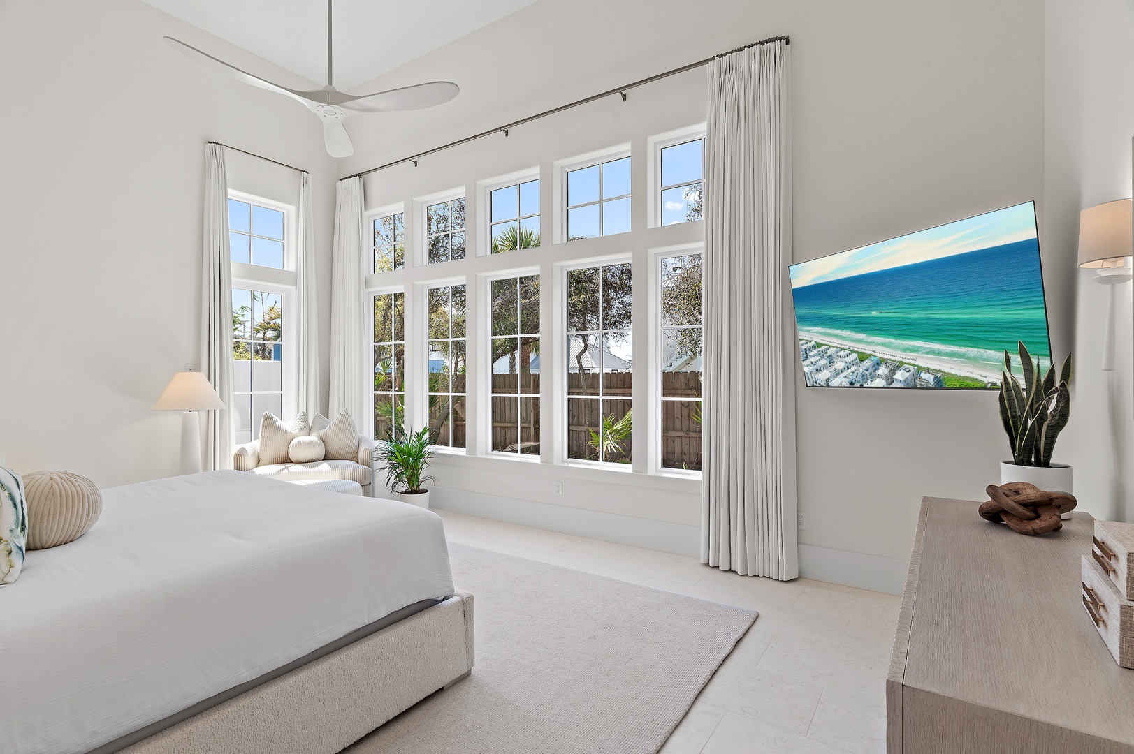 Wake up in this serene bedroom where sunlight pours through expansive windows and coastal art hints at the ocean beyond. Your peaceful retreat features high ceilings, a plush king bed, and a soothing all-white palette.