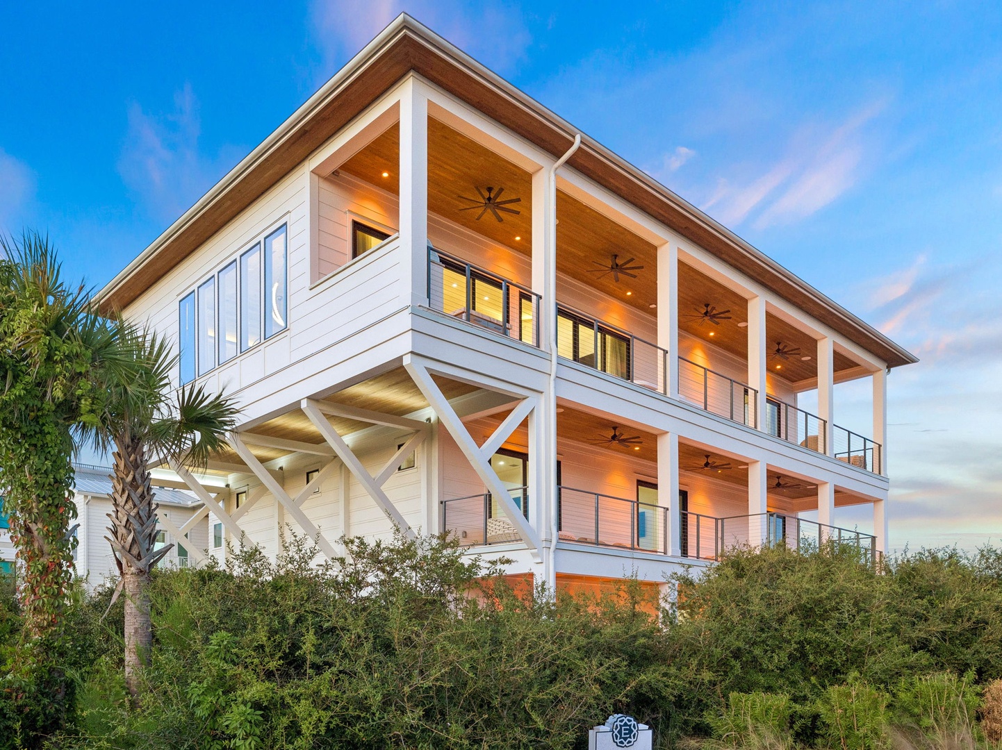 Modern coastal architecture with spacious balconies and warm lighting, perfectly positioned among lush tropical greenery near the shoreline.