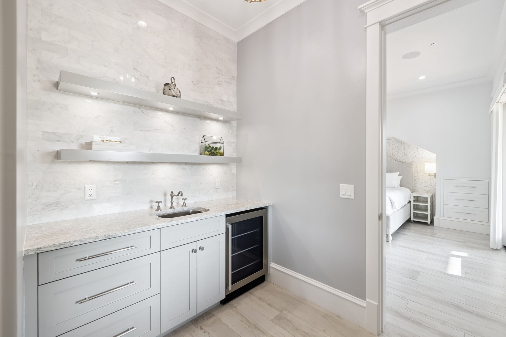 Your own private wet bar awaits with marble counters, built-in wine fridge, and elegant floating shelves for entertaining.