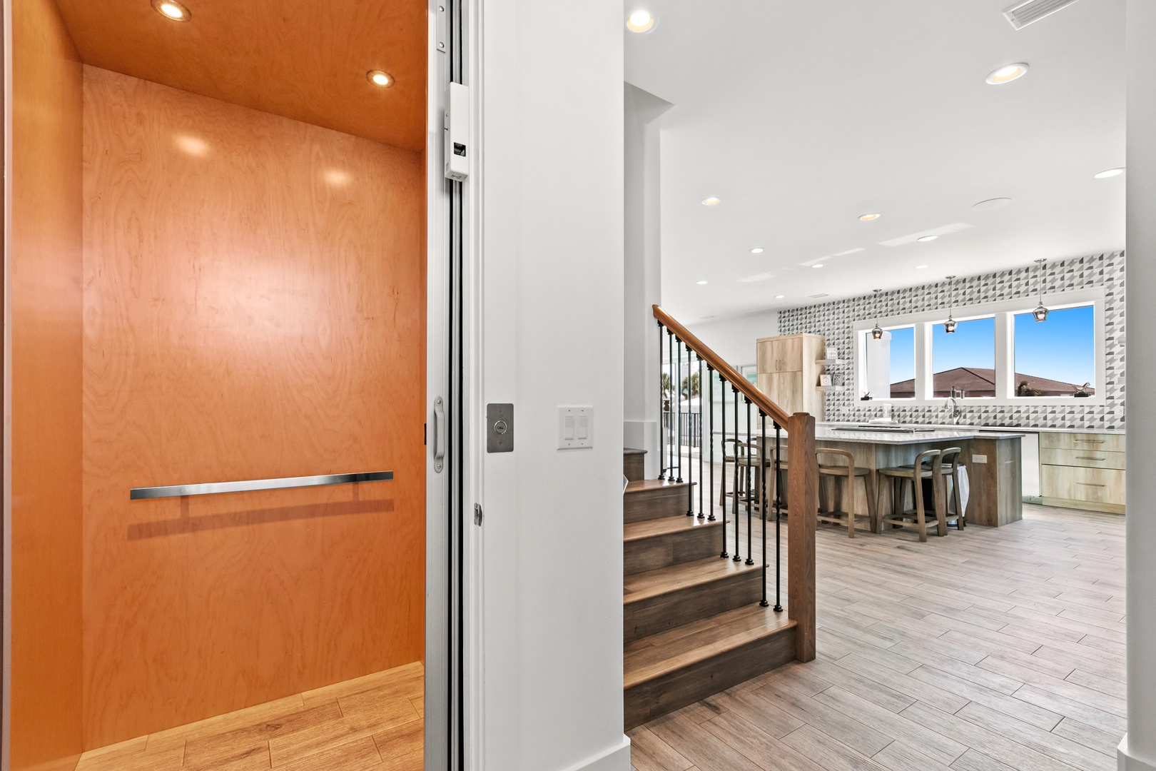 Step into a bright, inviting space where wood floors lead you past a sleek elevator and up a stylish stairway to open living and dining areas flooded with natural light.