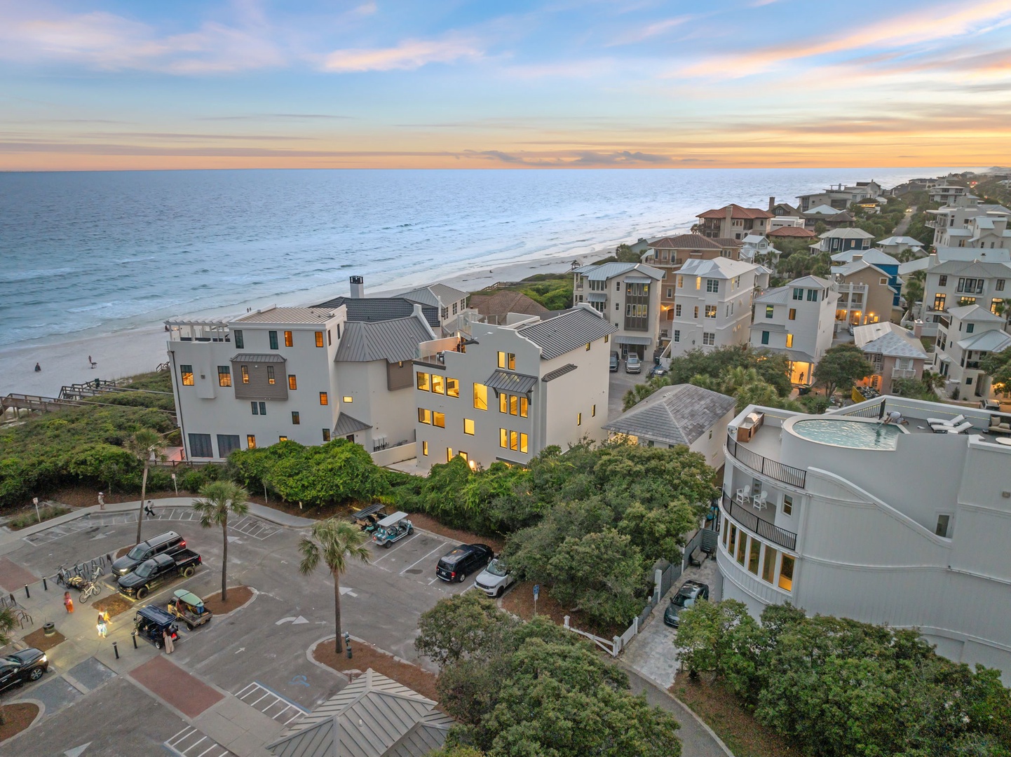 Elevated aerial view showcasing the beachfront property nestled in a coastal community, with ocean views and nearby parking. Captured during the golden hour of sunset.