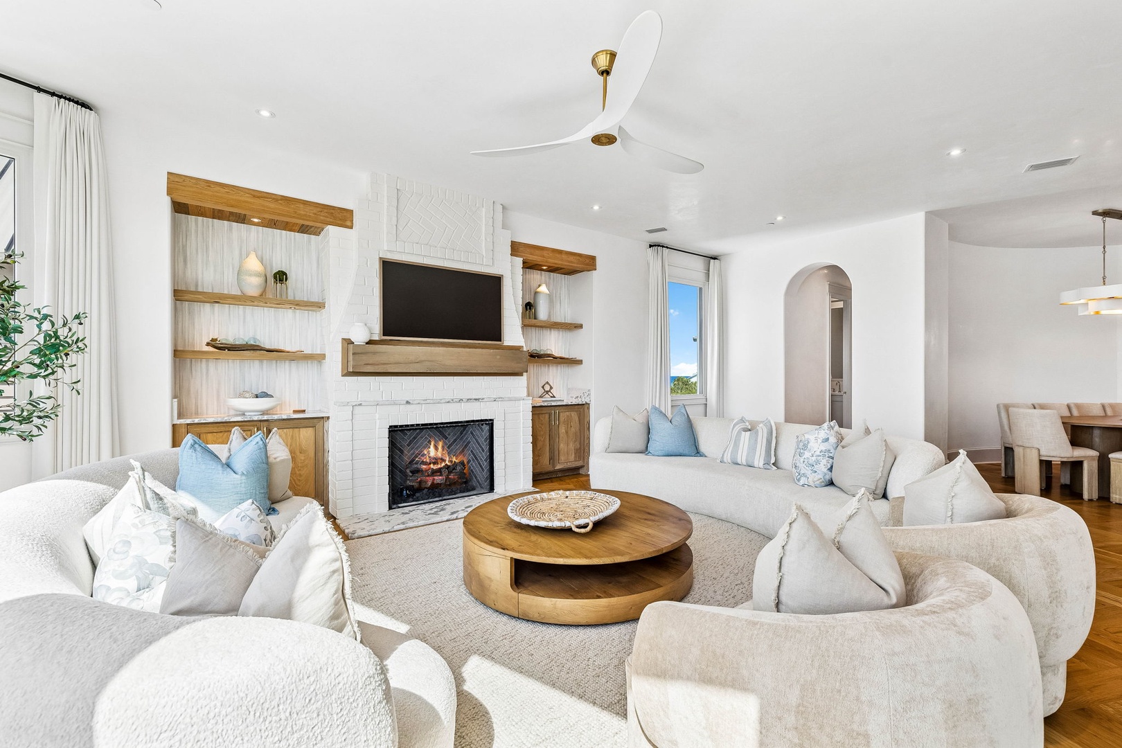 Sink into plush sofas and unwind by the fireplace in this bright, airy living space. Natural light, elegant shelving, and thoughtful touches create your perfect retreat.