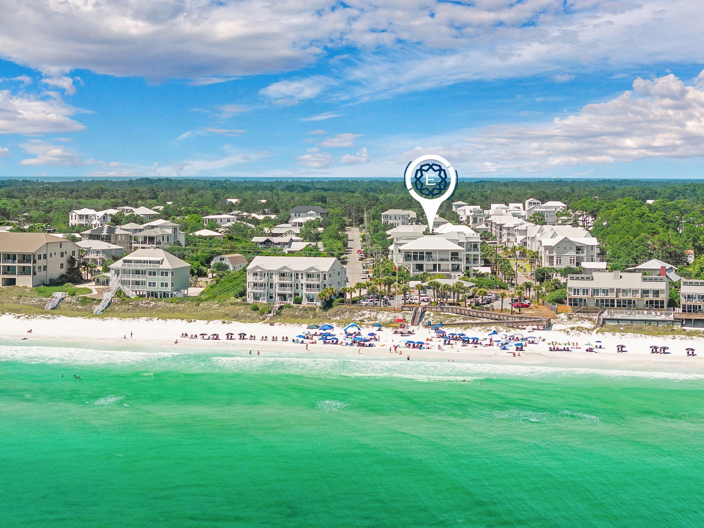 Aerial view of a coastal neighborhood with white-sand beach and turquoise Gulf waters, surrounded by residential properties and lush greenery.