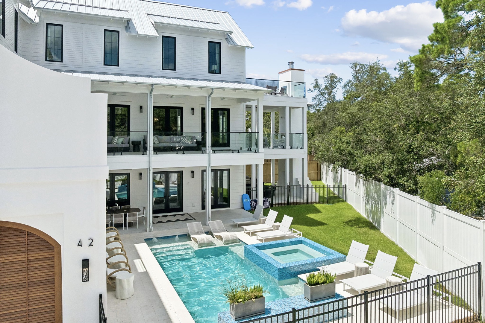 A modern multi-story property featuring a private pool and hot tub surrounded by manicured grounds, offering an elegant outdoor retreat with plenty of space to relax and unwind.