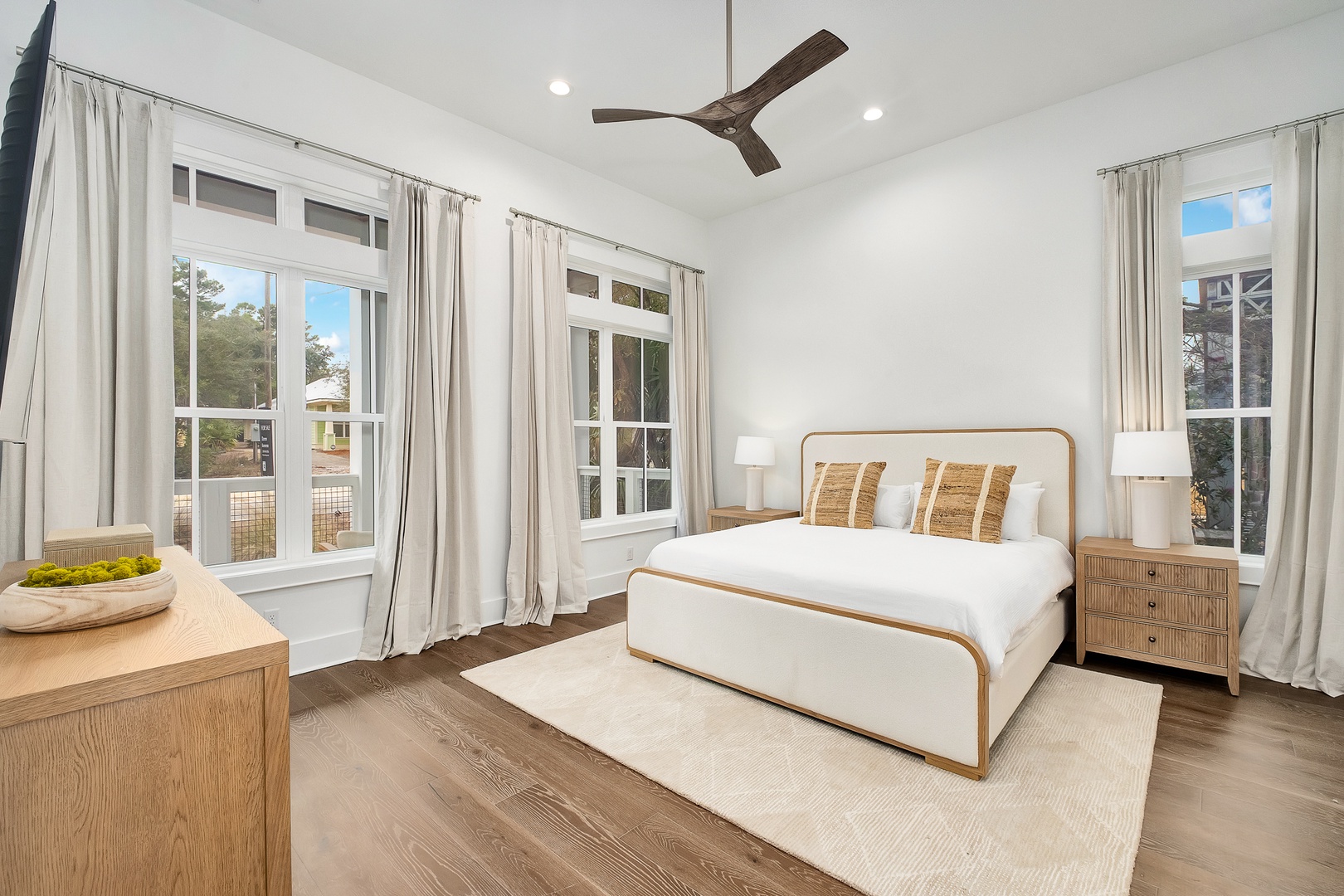 Sink into crisp white linens and natural textures in your serene bedroom, where gentle breezes from the ceiling fan create perfect sleeping comfort.