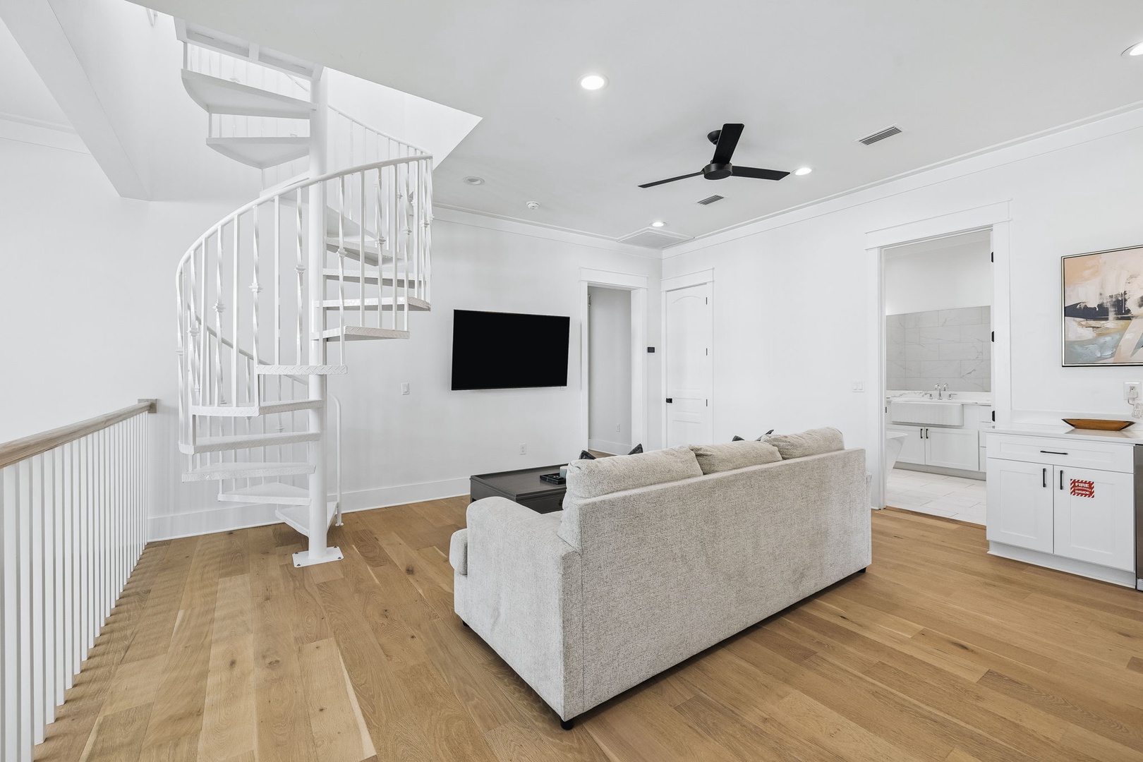 Step into a bright, open living space featuring warm wood floors, a cozy sofa, and a striking spiral staircase leading to your private loft above. The sleek kitchenette keeps refreshments within reach while you unwind.