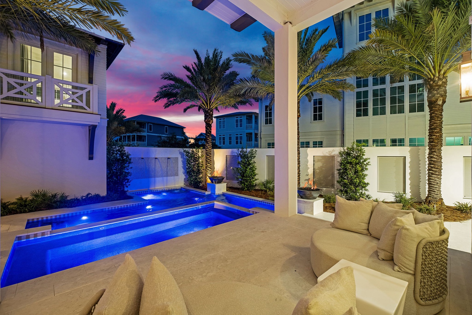 A stunning backdrop of palm-lined architecture frames the illuminated pool area during a vibrant dusk, offering a private tropical retreat in a beautifully designed residential setting.