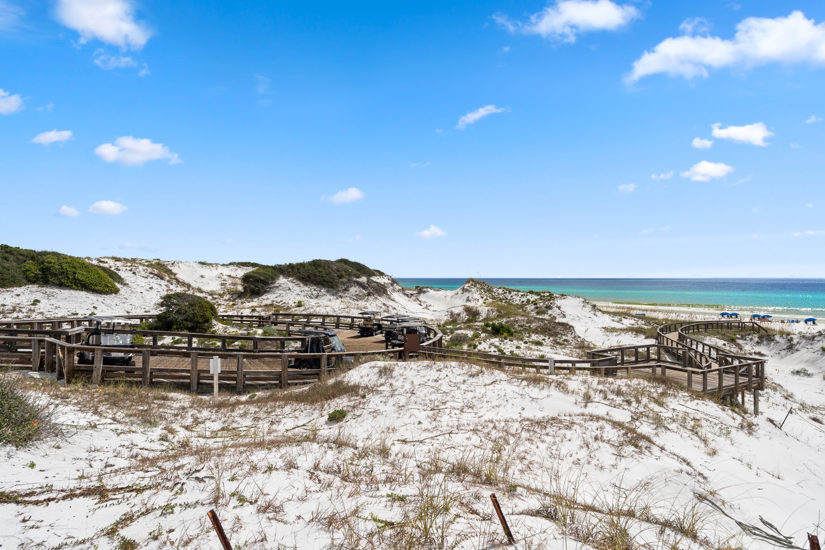 Coastal beach access features winding boardwalks through pristine white sand dunes, leading to turquoise waters and scenic shoreline views.