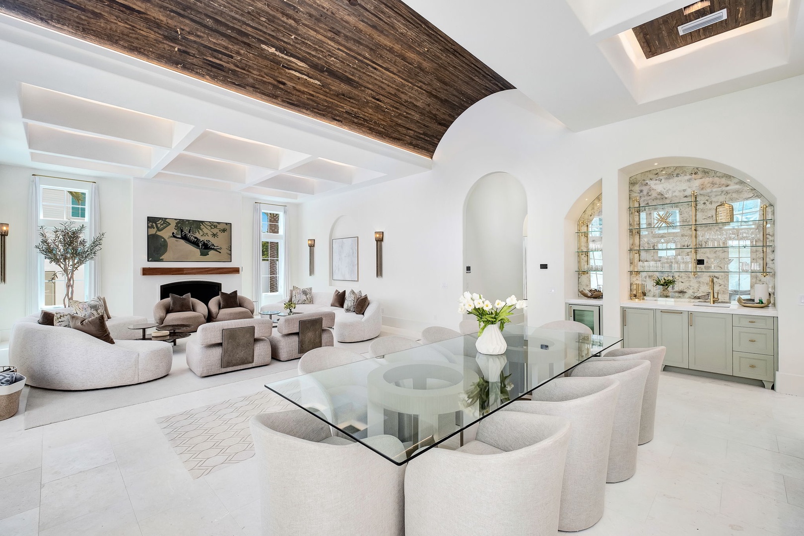 Settle into plush seating beneath stunning wood-beam ceilings while natural light floods this elegant space. Gather around the glass dining table or sink into the curved sofas, surrounded by sophisticated coastal charm and thoughtful details.