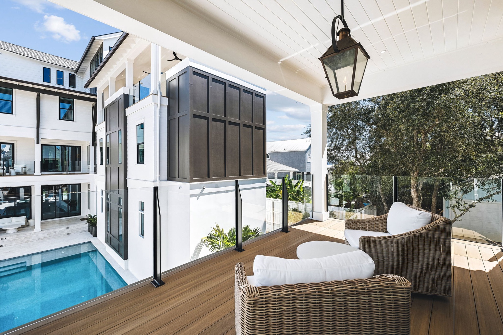 Modern vacation rental building with sleek outdoor entertaining areas, blue tile pool, covered patio seating, and natural greenery on property grounds.