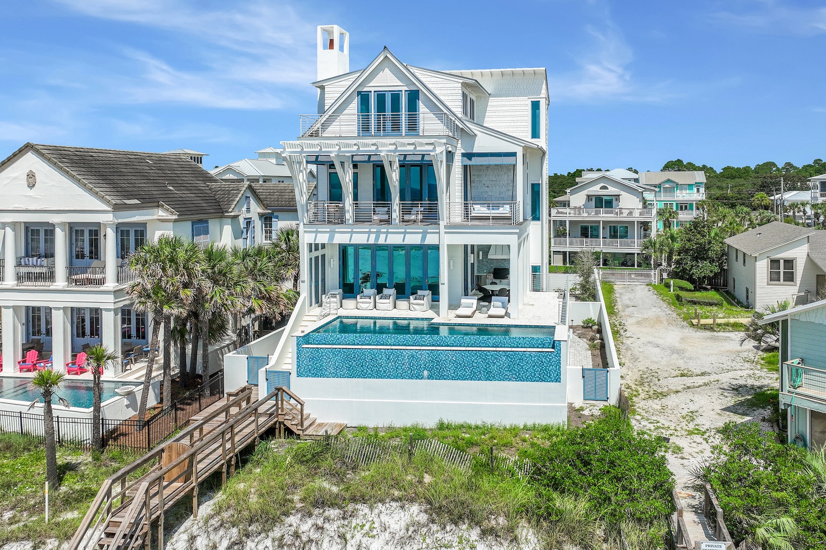 A stunning beachfront property featuring elegant coastal architecture and a sparkling infinity pool overlooking the shore. The multi-level home sits in a picturesque residential beach community.