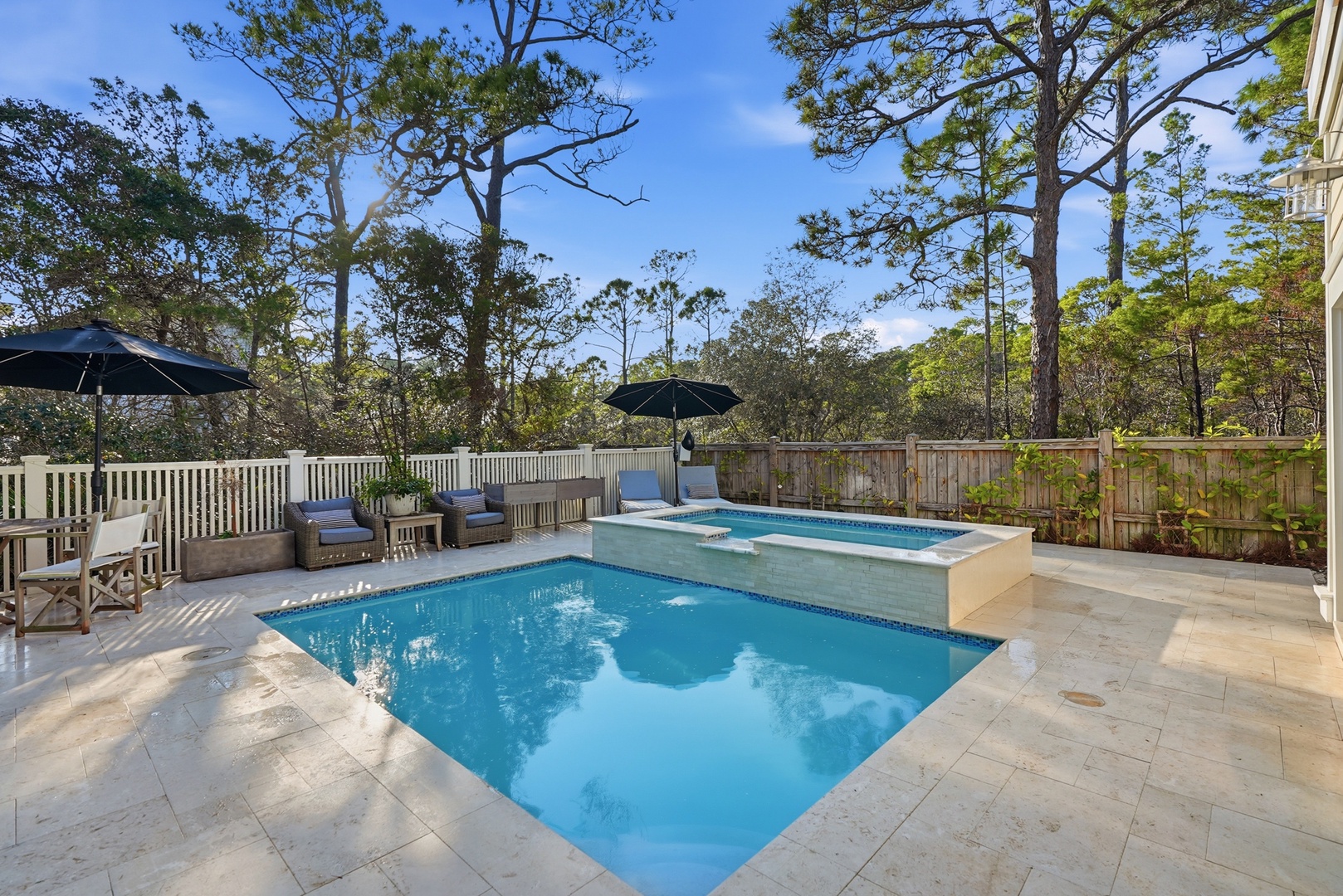 Dive into your private pool and hot tub oasis, framed by towering pines and bright blue skies. Lounge under umbrellas with a cool drink, soaking in the warmth and serenity of this secluded outdoor retreat.