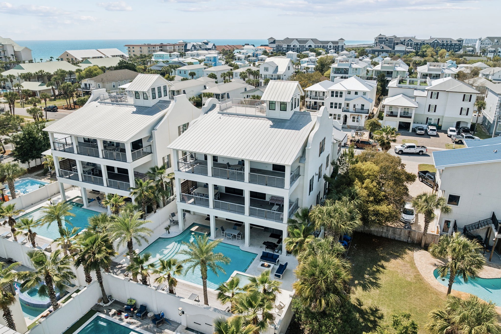Aerial view of luxury beachfront vacation rentals featuring pristine pools, palm trees, and white sand beaches in a coastal resort community.
