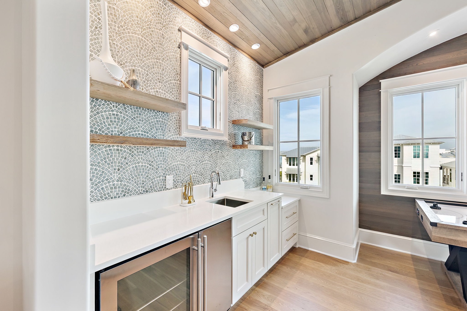 Your stylish butler's pantry gleams with intricate mosaic tile and natural wood shelving, offering a functional yet beautiful prep space with refreshing coastal views.