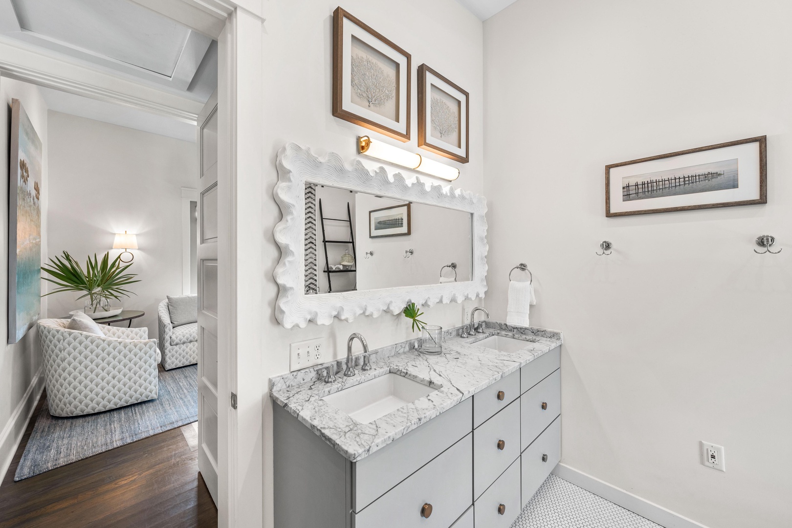 Refresh in your elegant dual-sink bathroom featuring marble countertops, stylish scalloped mirror, and thoughtful coastal touches.