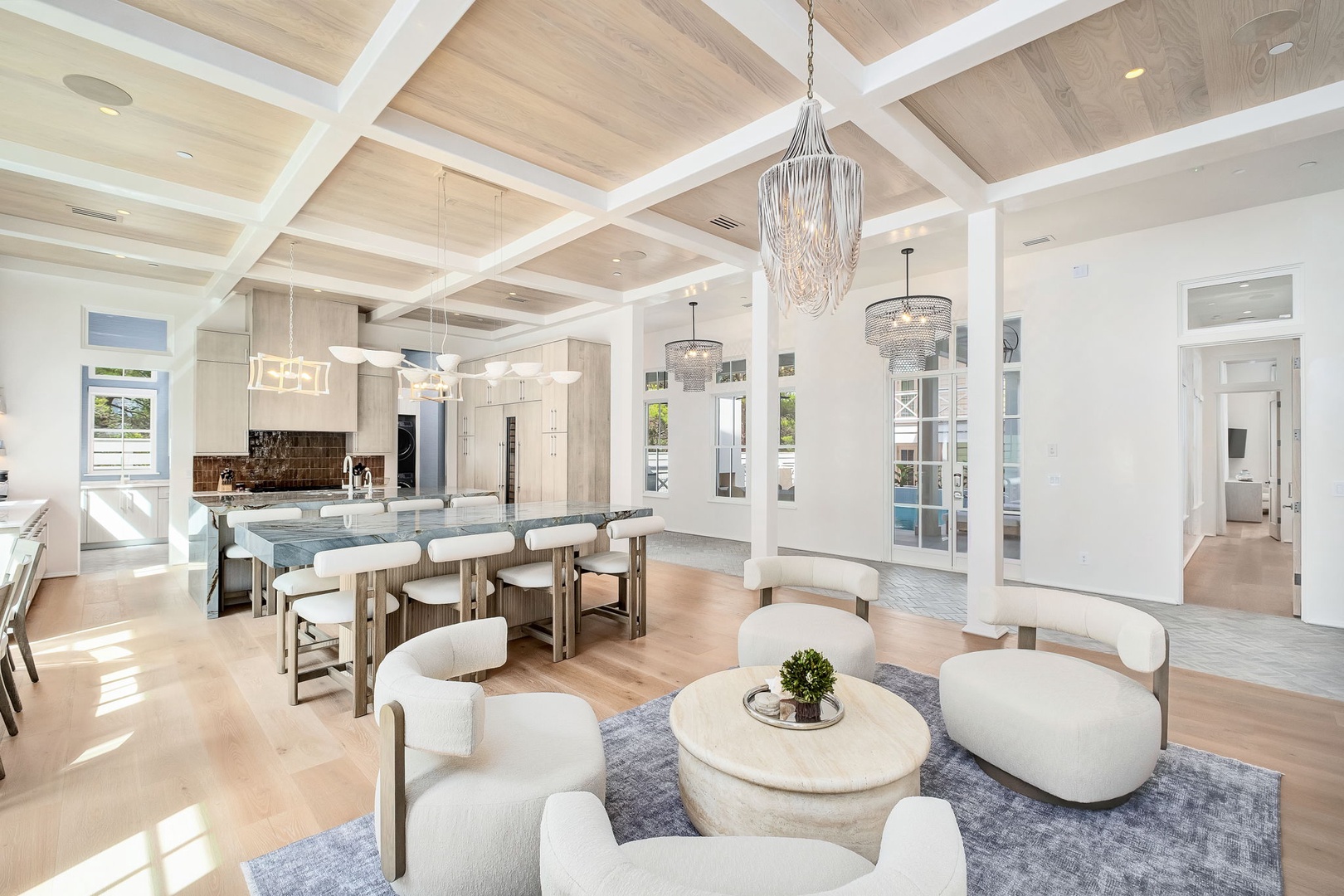 Stunning open-concept living with soaring beamed ceilings and elegant chandeliers. Floor-to-ceiling windows flood the space with light, illuminating designer furnishings perfect for gatherings or relaxation.