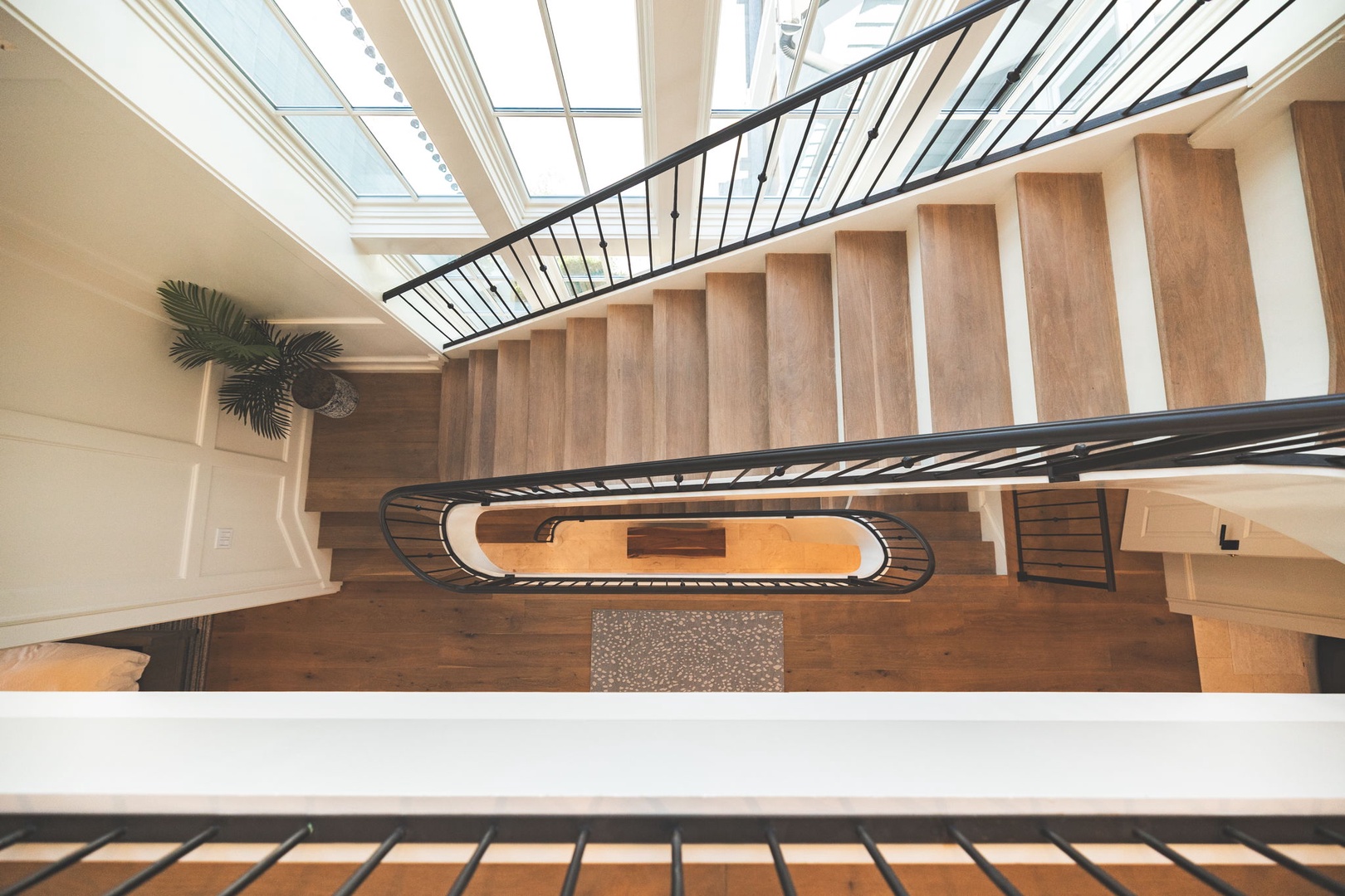 An elegant staircase spirals gracefully through your vacation home, flooded with natural light from overhead skylights. Warm wood steps and sleek metal railings create an inviting architectural centerpiece.