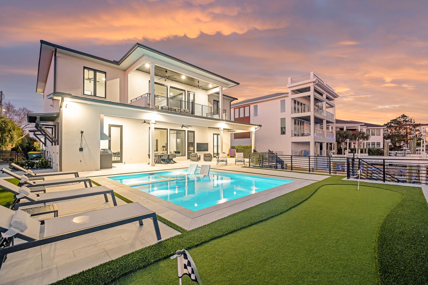 Modern luxury home featuring sleek architecture with contemporary pool and manicured lawn under stunning sunset skies.