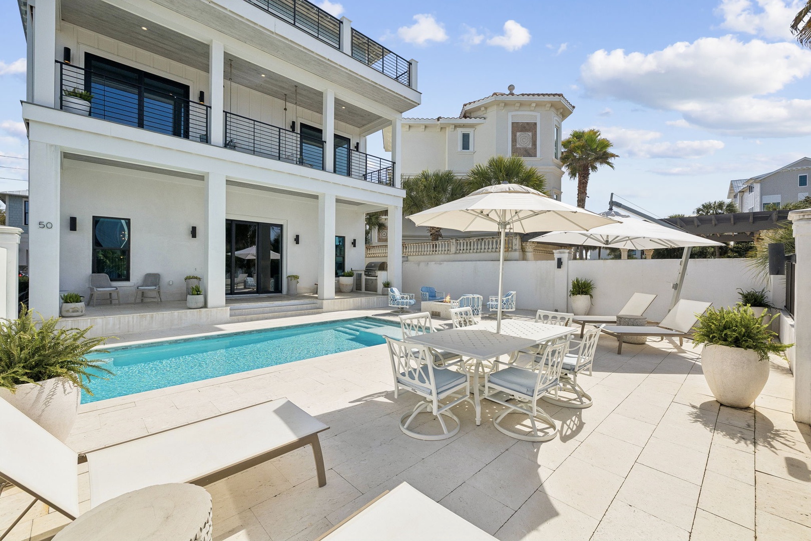 Modern beachside villa featuring a pristine pool, elegant patio dining, and multiple balconies overlooking the coastal neighborhood.