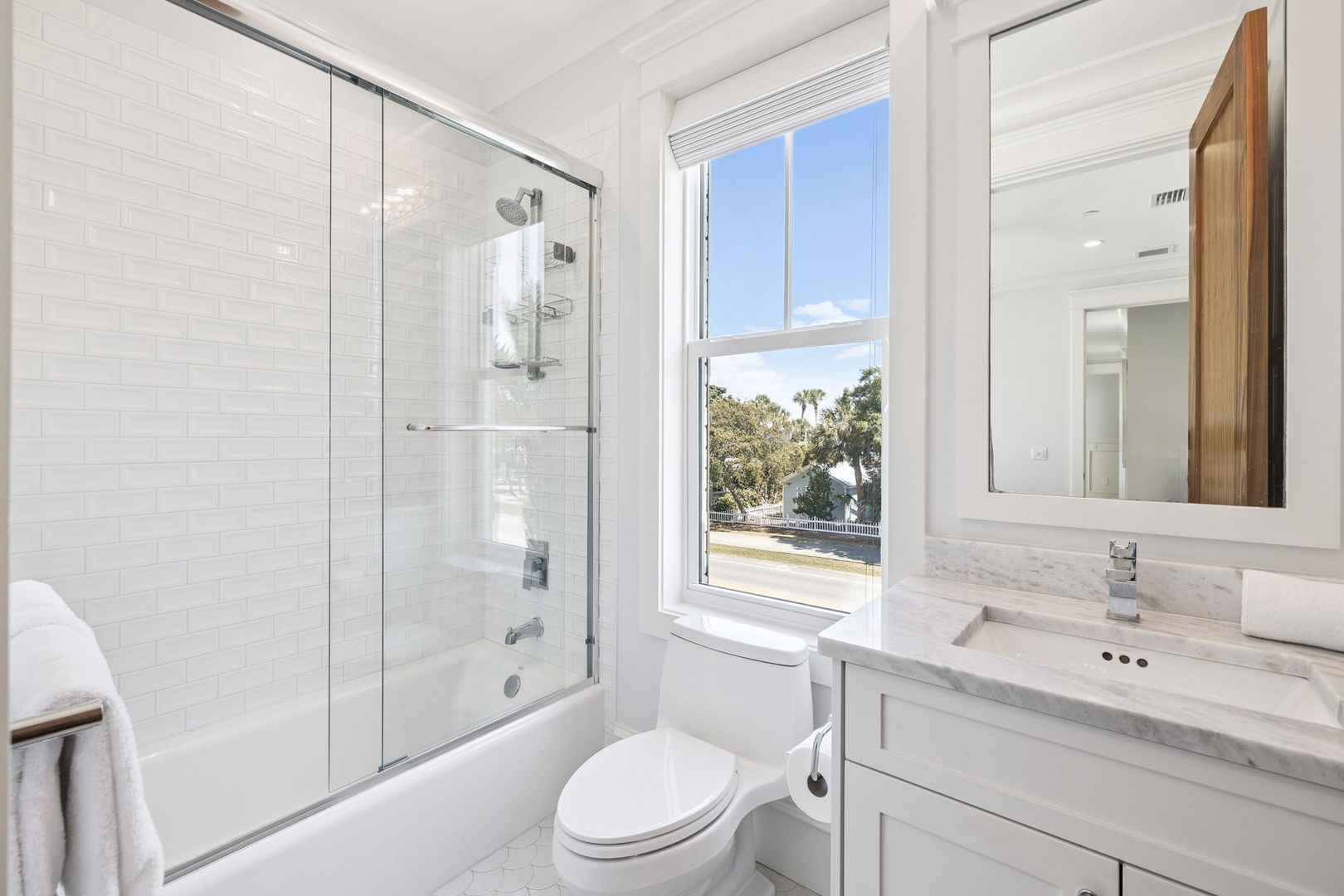 Unwind in your sleek marble bathroom featuring a luxurious soaking tub and rainfall shower, all bathed in natural light from the scenic window view.