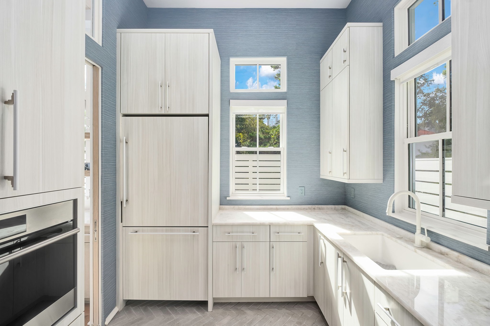 Bright, airy kitchen with soaring ceilings, natural light, calming blue textured walls, and clean white cabinetry—a fresh, modern space that's both functional and inviting.