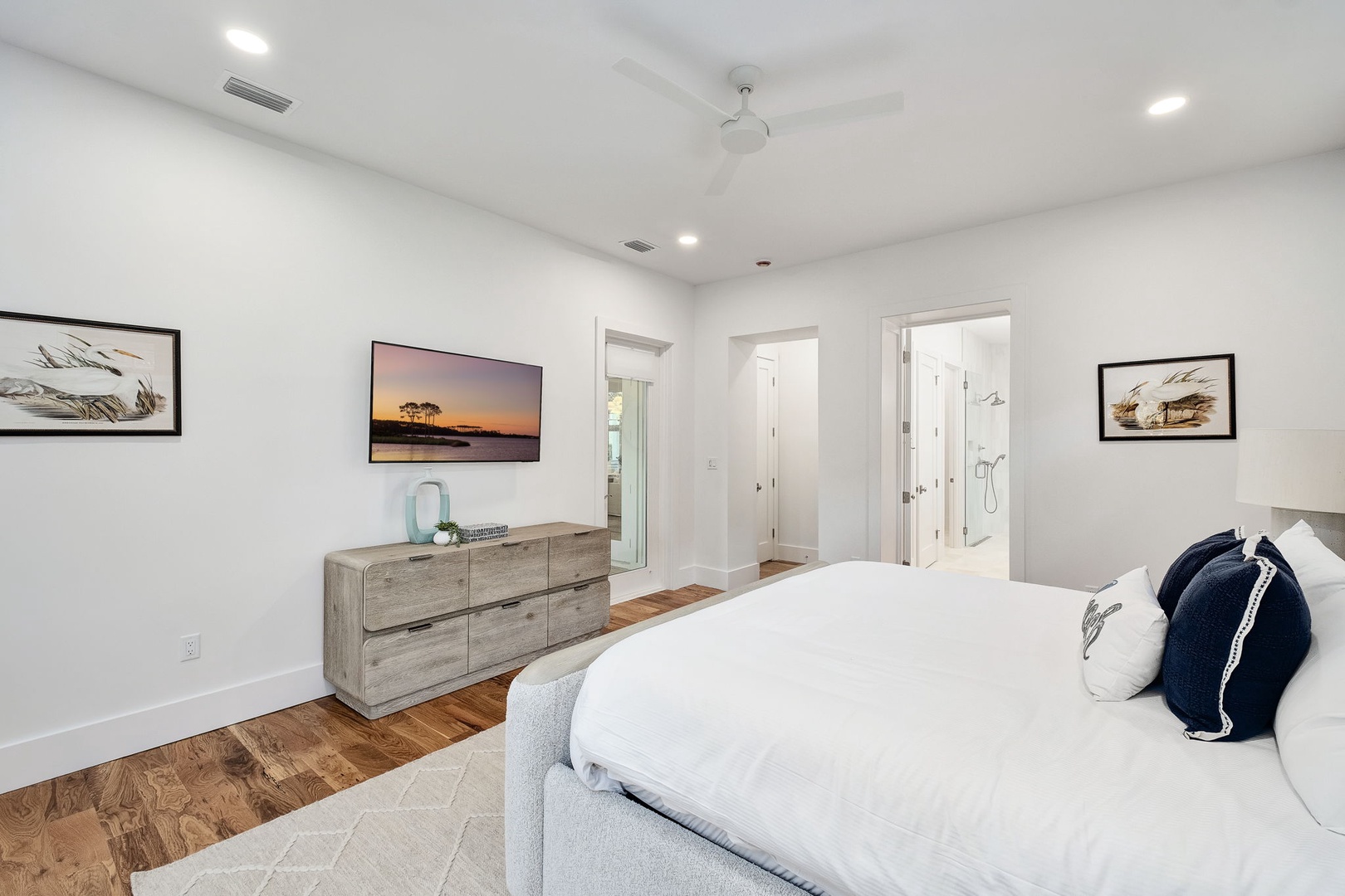 Your master bedroom offers crisp white linens, warm wood floors, and coastal artwork that creates a serene retreat after your adventures.