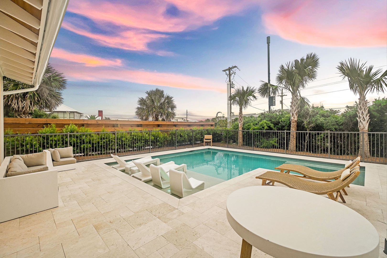 A striking sunset paints the sky in pastel hues above the private pool area, framed by swaying palms and surrounded by comfortable lounge spaces perfect for evening relaxation.
