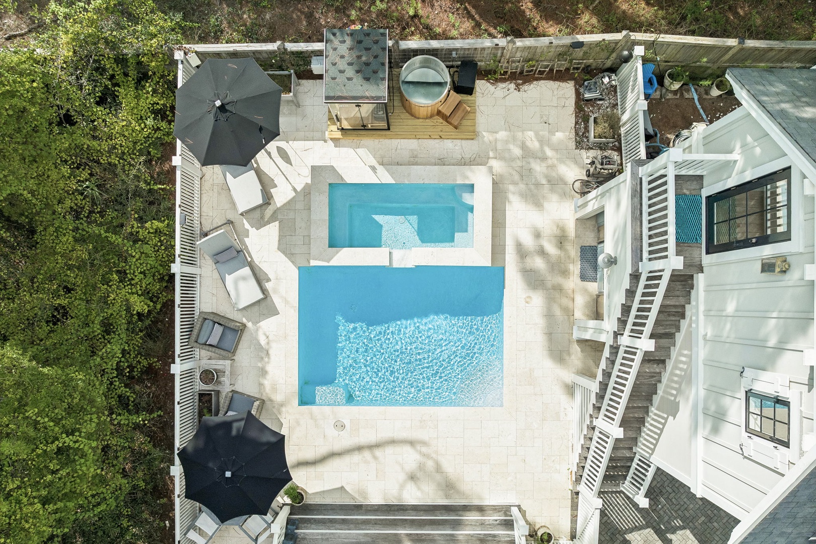 An aerial perspective reveals the property's private pool and spacious outdoor deck, complete with lounge chairs, a hot tub, and a patio umbrella. The home is nestled within a peaceful, tree-lined setting.