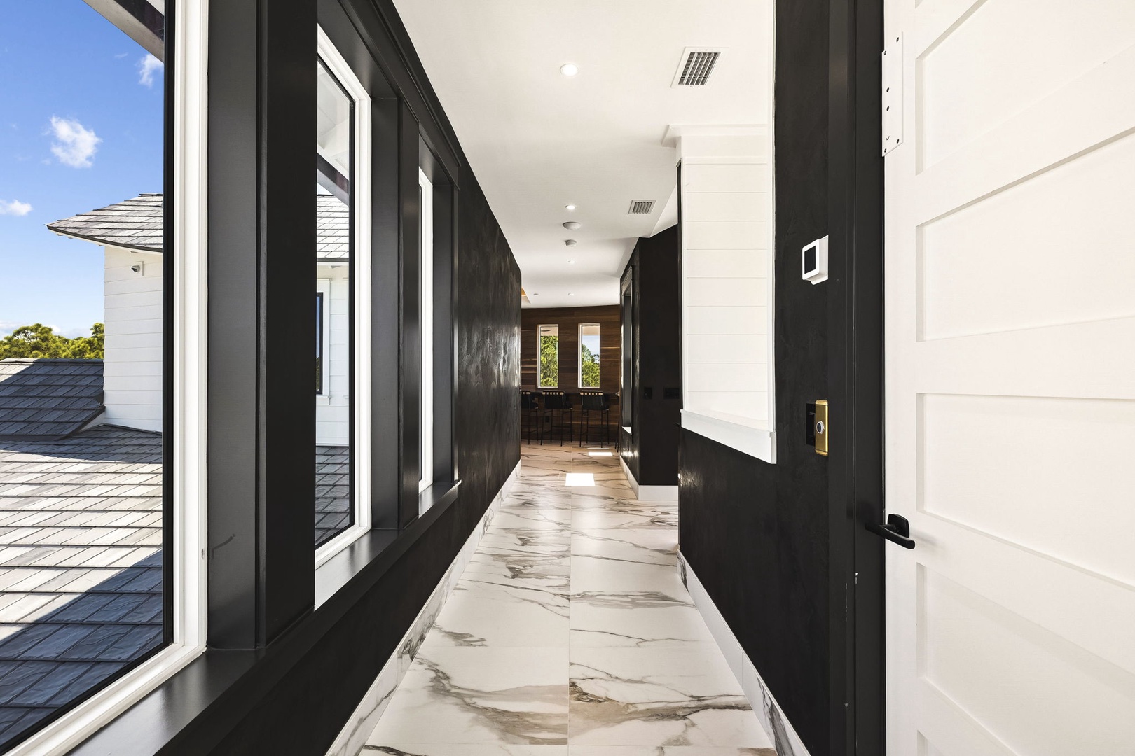 An elegant entrance hallway welcomes you with polished marble flooring and dramatic floor-to-ceiling windows, flooding the space with natural light and offering glimpses of lush greenery outside.