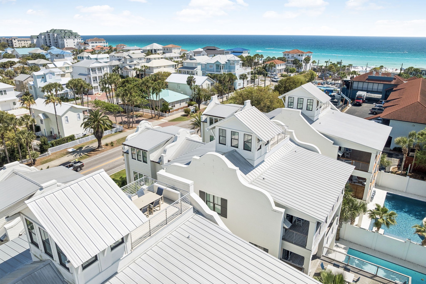 Aerial view showcasing a stunning beachfront property nestled among pristine coastal homes with turquoise waters and white sand beaches just steps away.