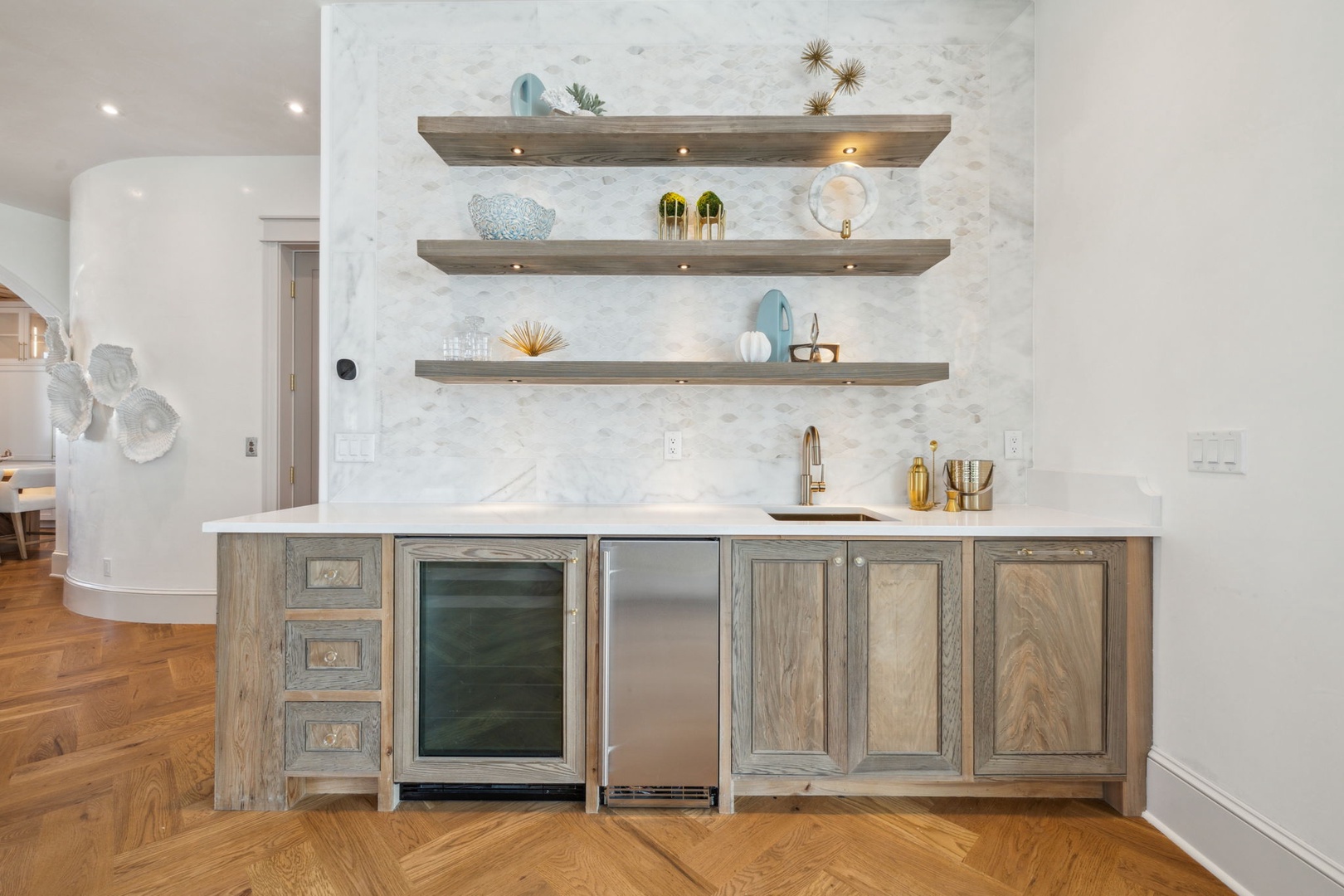 Your stylish wet bar features a marble backsplash, warm wood shelving with under-lighting, a sink, and both beverage cooler and mini fridge for easy entertaining.