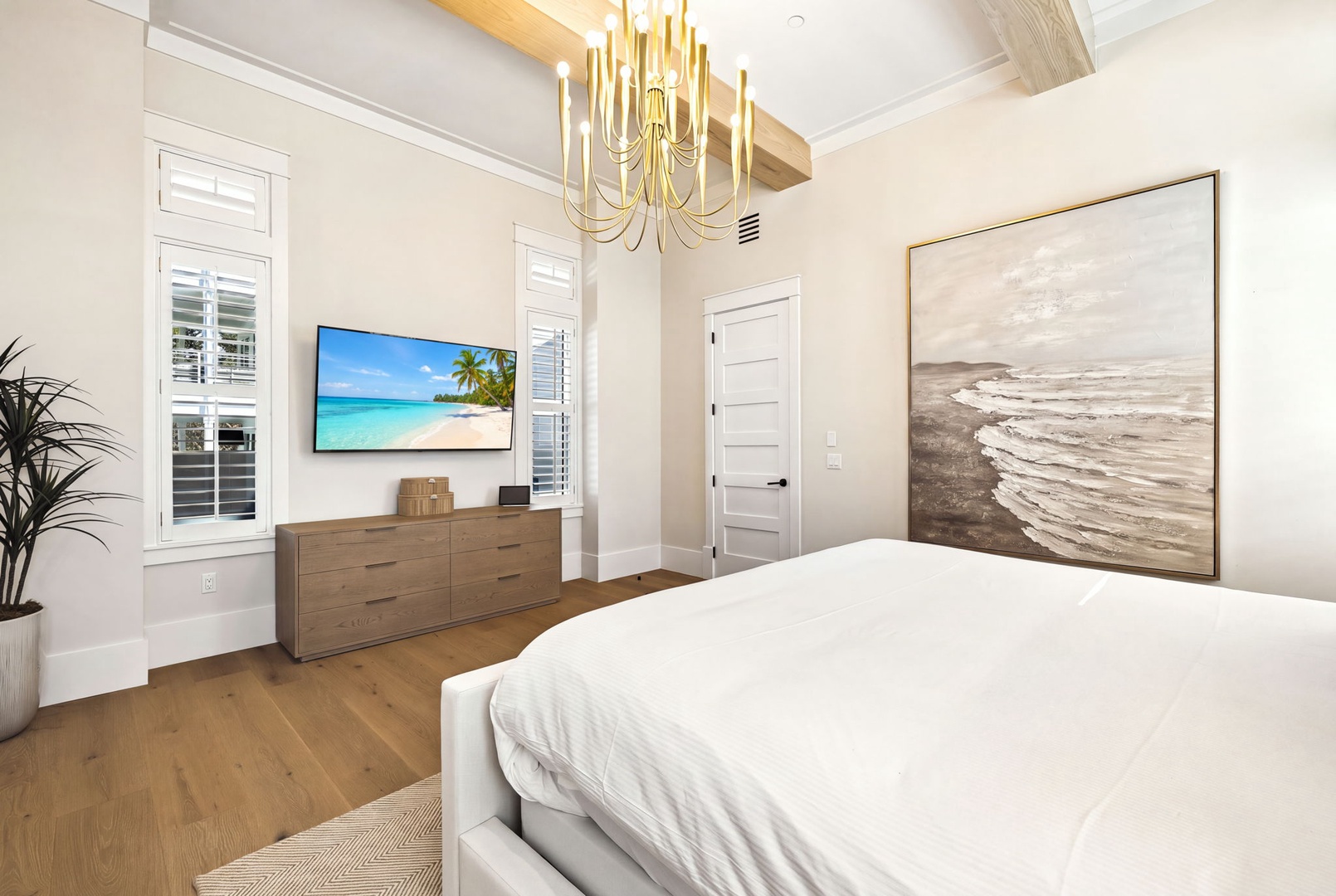 Sink into crisp linens under a statement chandelier, with coastal artwork and warm wood tones creating your serene escape. Natural light pours through plantation shutters, making mornings feel effortless.