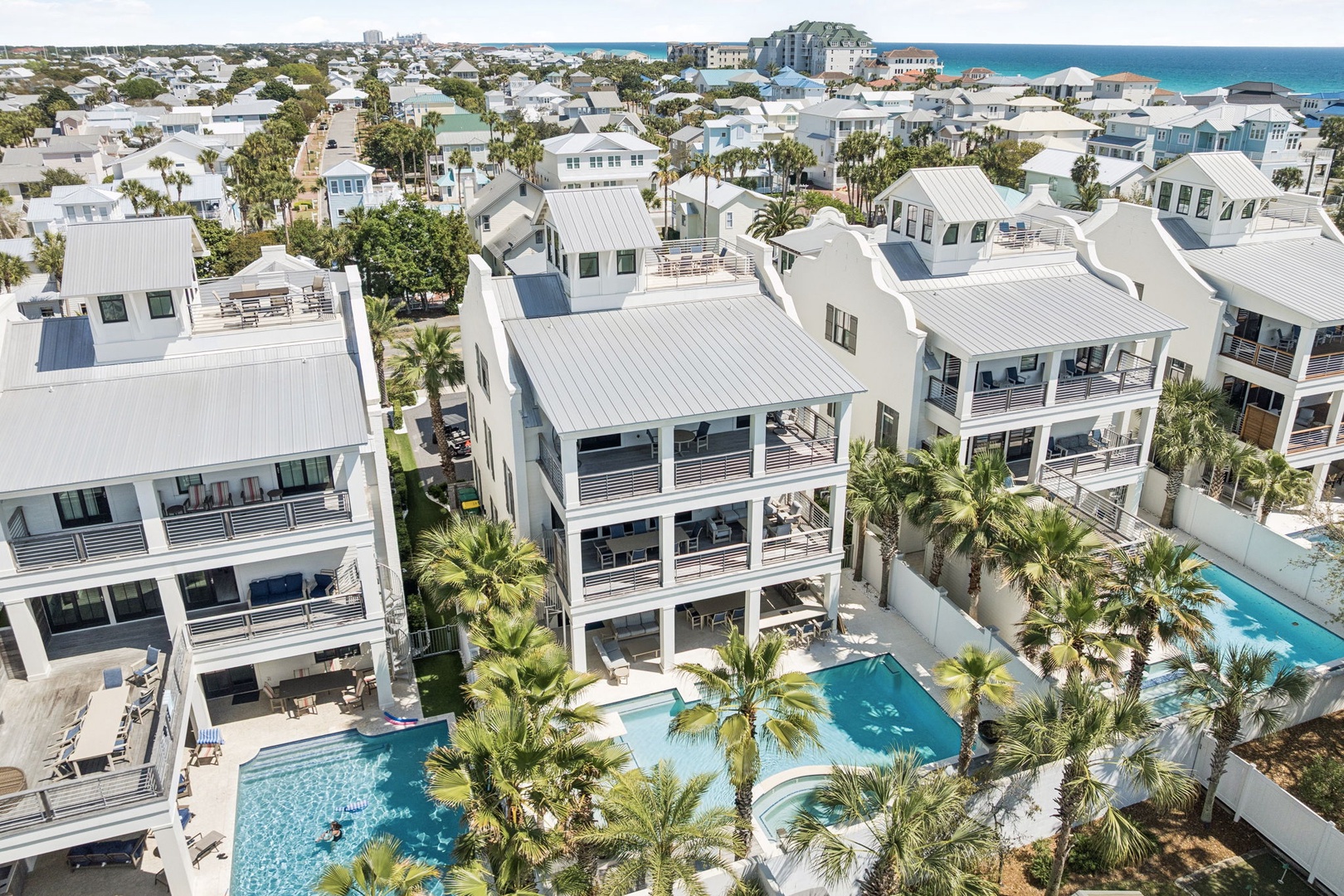 Aerial view of luxury beachside vacation homes featuring private pools, palm trees, and modern coastal architecture in this exclusive resort community.