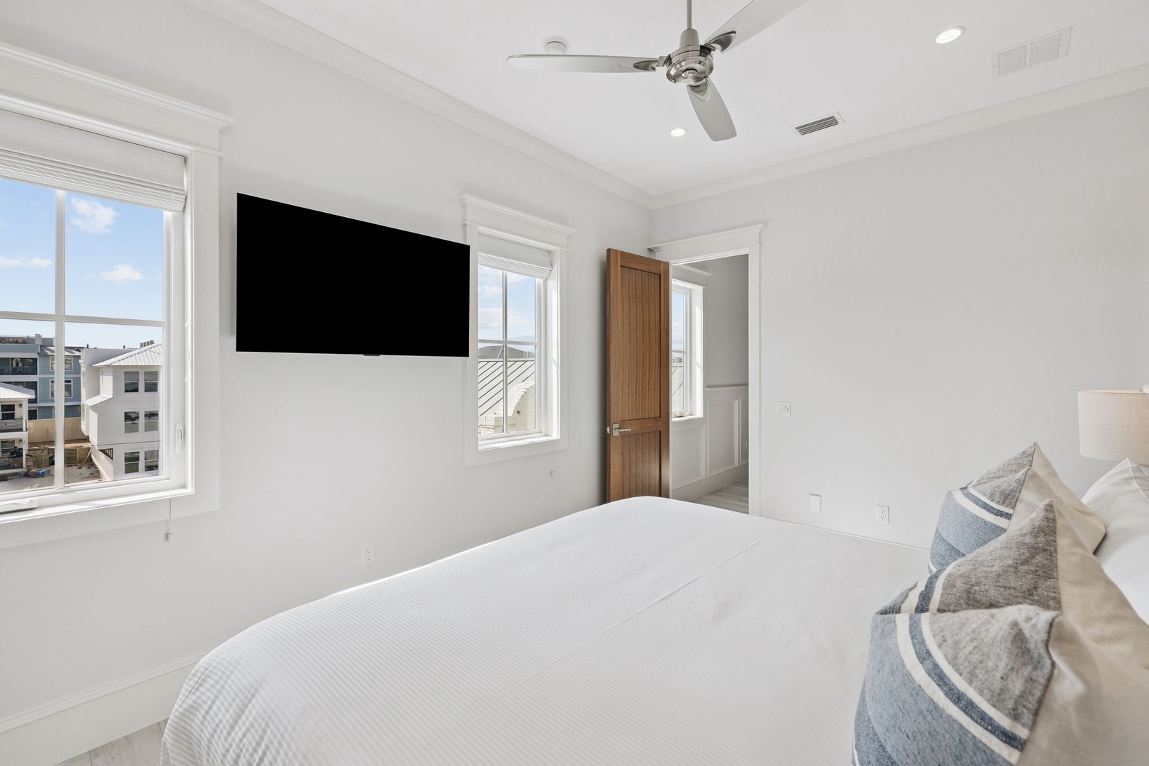 Sink into crisp white linens in your serene bedroom, where natural light floods through large windows and a wall-mounted TV awaits your evening entertainment.
