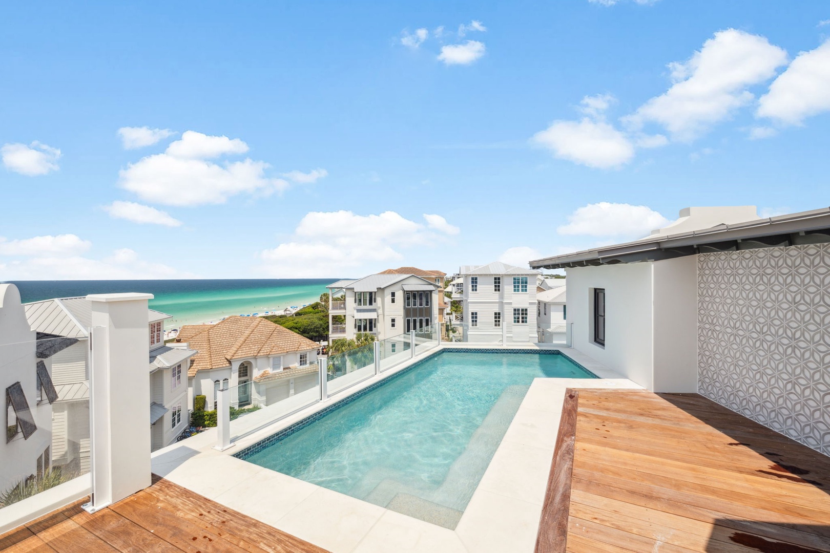 Rooftop pool overlooks the emerald coastline and neighboring homes, offering a private retreat with warm wooden decking and stunning sea views.