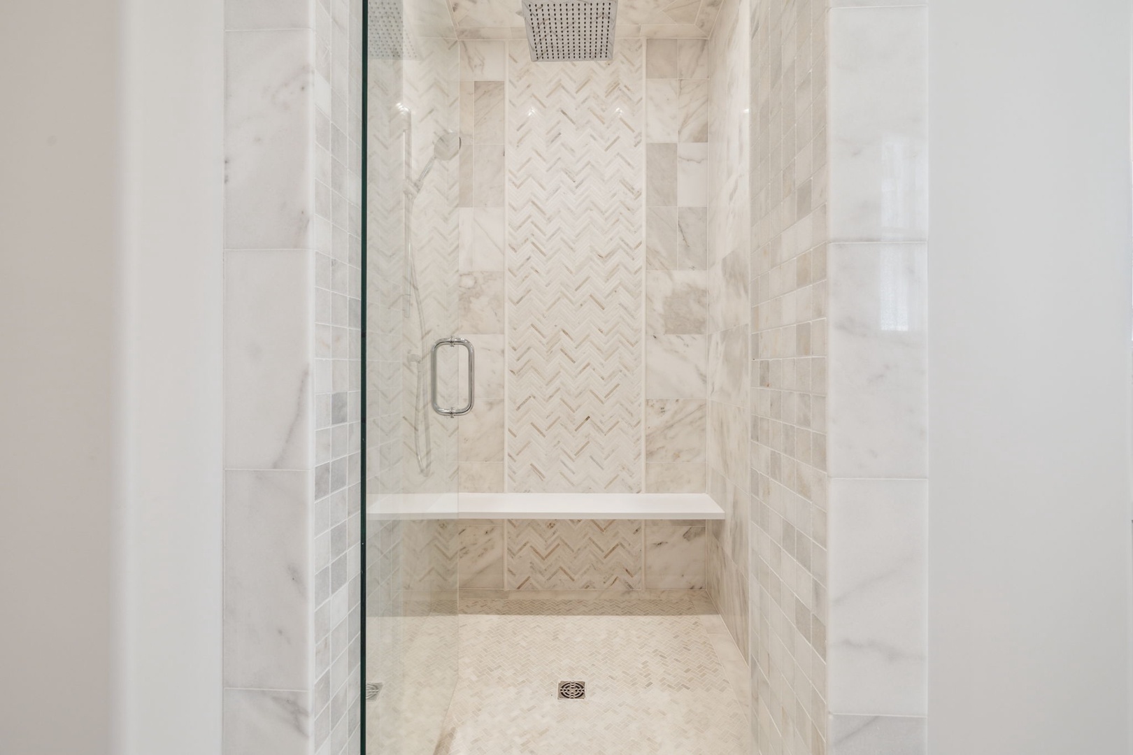 Luxurious herringbone marble tiling and a rain showerhead create your private spa escape. The built-in bench offers comfort as you unwind under the soothing water.