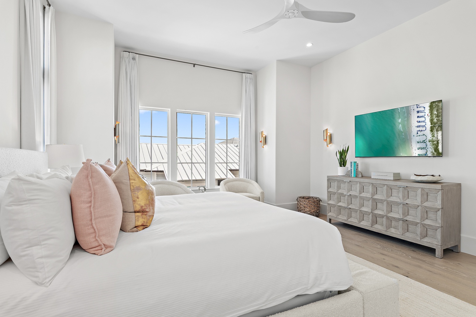 Sink into crisp white linens in your serene bedroom, where balcony doors frame coastal views and modern beach-inspired decor creates your perfect retreat.
