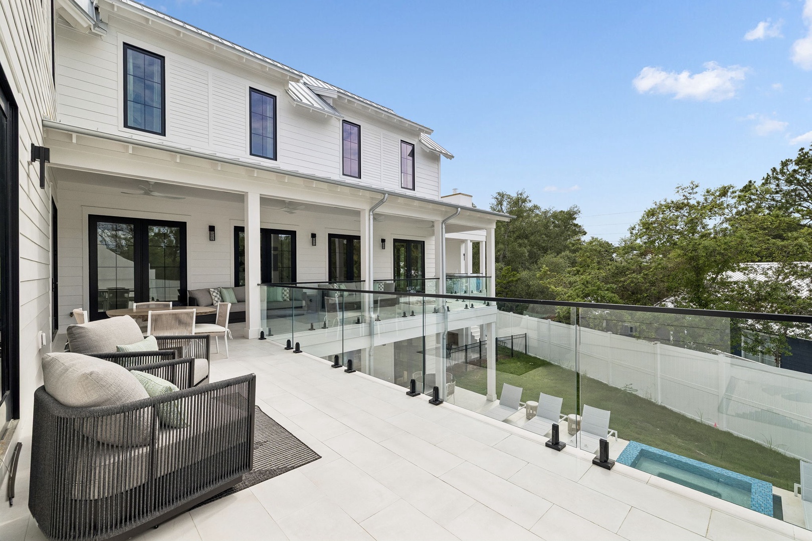 Modern two-story property featuring clean white siding, black-framed windows, and expansive covered porch with glass railings overlooking lush treetops and manicured grounds below.