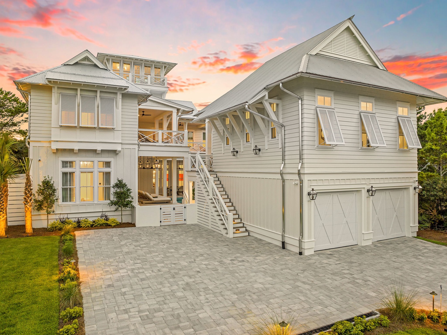 A stunning coastal retreat with classic architectural charm, bathed in the warm glow of sunset. The property features elegant outdoor staircases and a spacious paved courtyard perfect for arrival.
