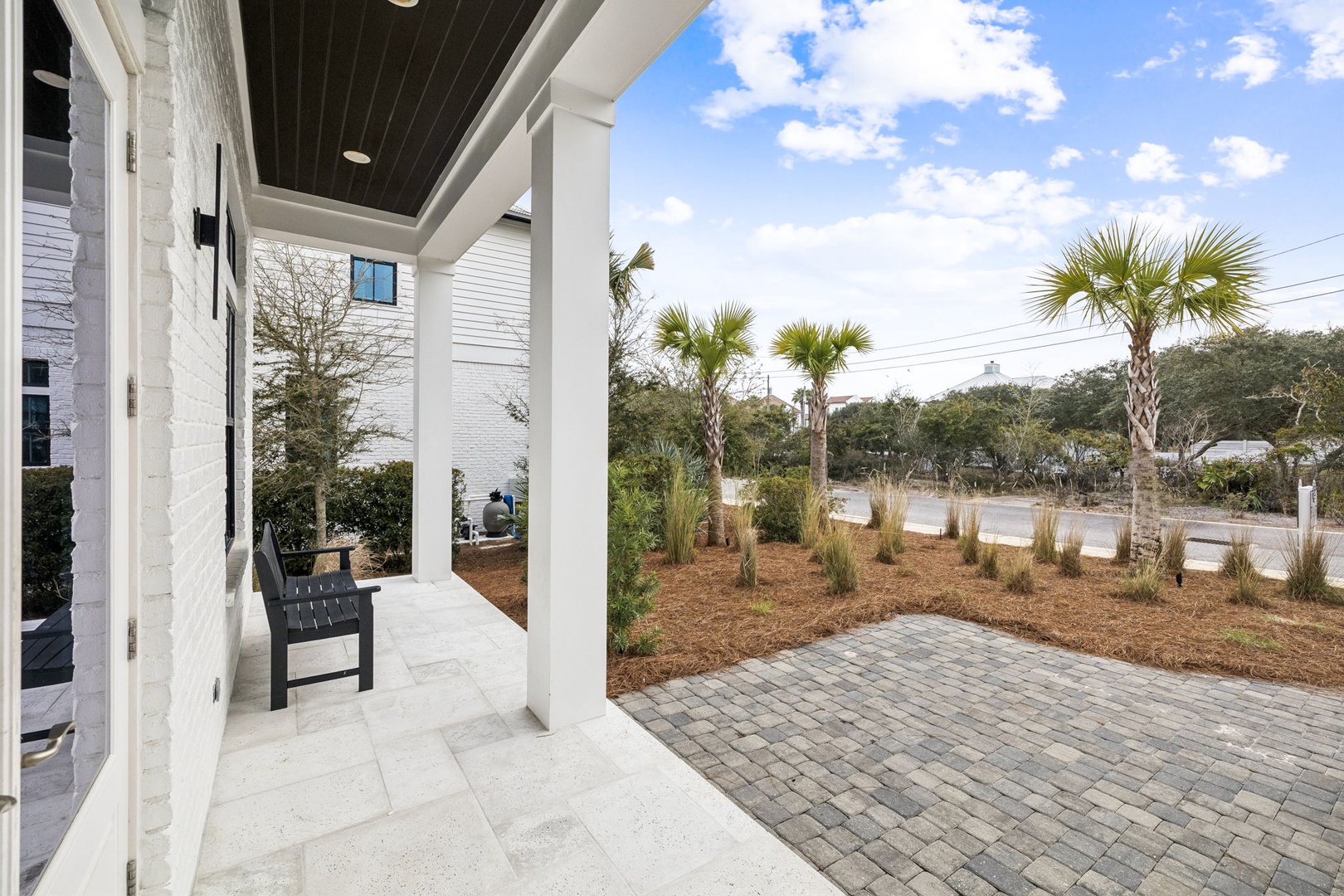 Modern coastal property featuring covered porch with seating and tropical landscaping including palm trees and native plantings.