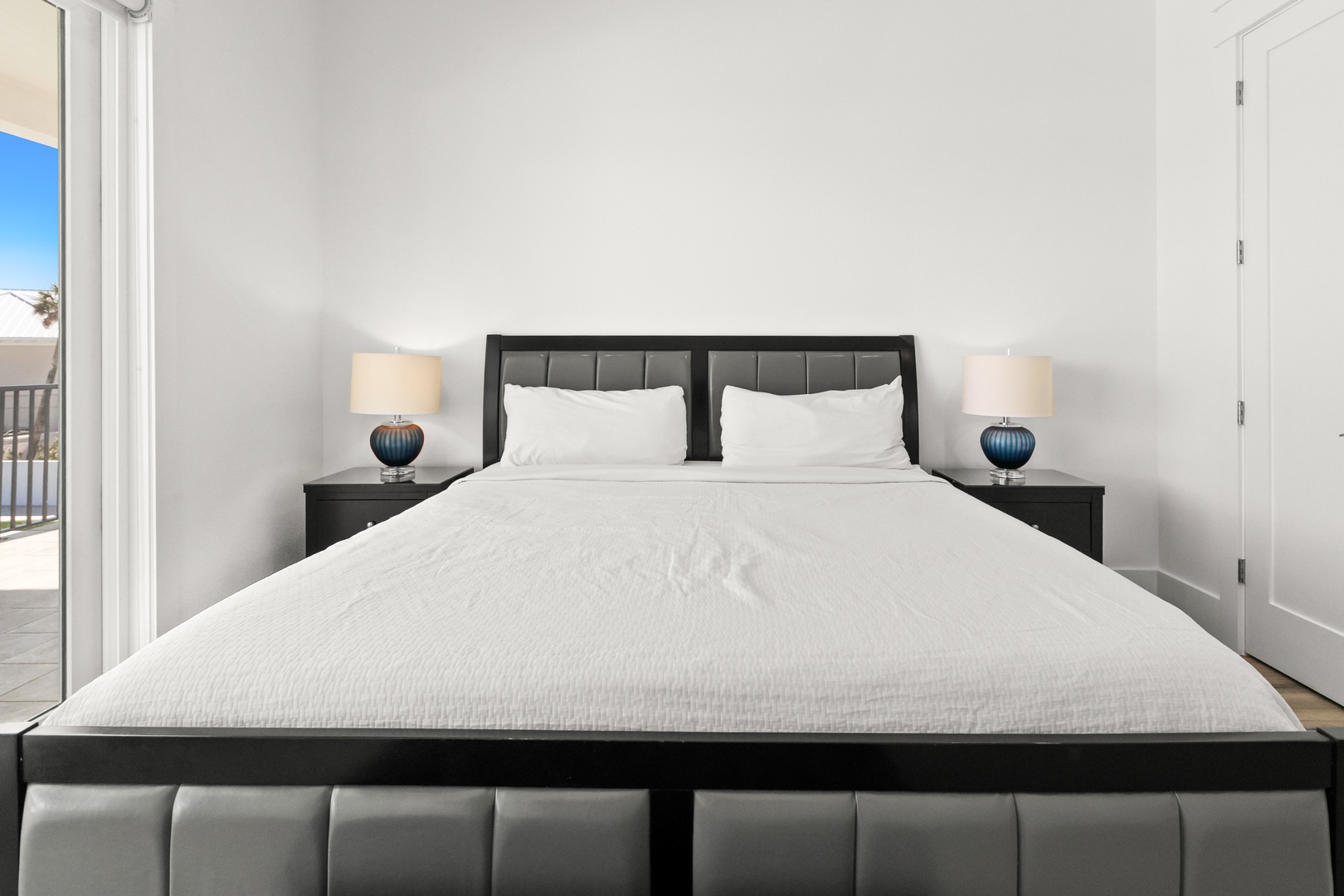 Sink into plush white linens and wake to soft natural light streaming through your balcony door. Modern nightstands and sleek lighting frame your restful retreat.