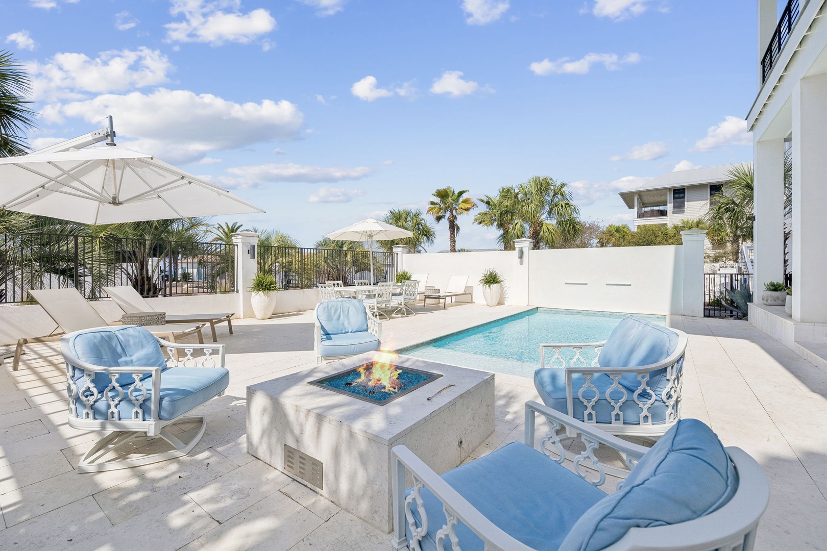 Relax in your private poolside paradise with elegant blue seating, fire feature, and tropical palm views under endless skies.