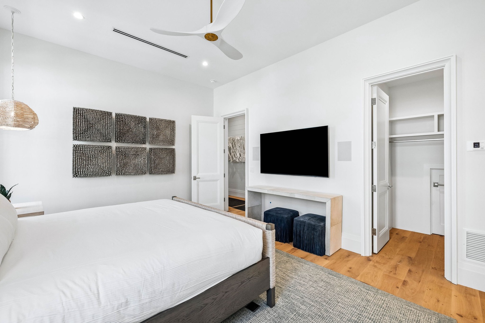 Unwind in your serene bedroom featuring a plush bed, coastal-inspired decor, and sleek entertainment setup. High ceilings and natural wood floors create an airy, relaxing retreat perfect for restful nights.