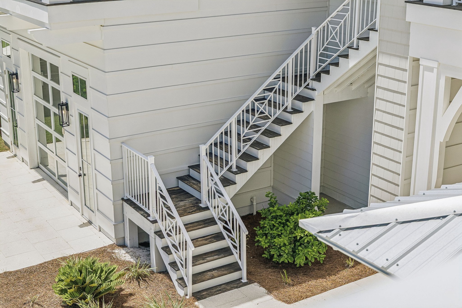 The property features clean architectural lines with crisp white exterior siding, decorative shutters, and charming outdoor stairways connecting multiple levels. Small landscaped planters add a touch of greenery to the coastal-inspired design.