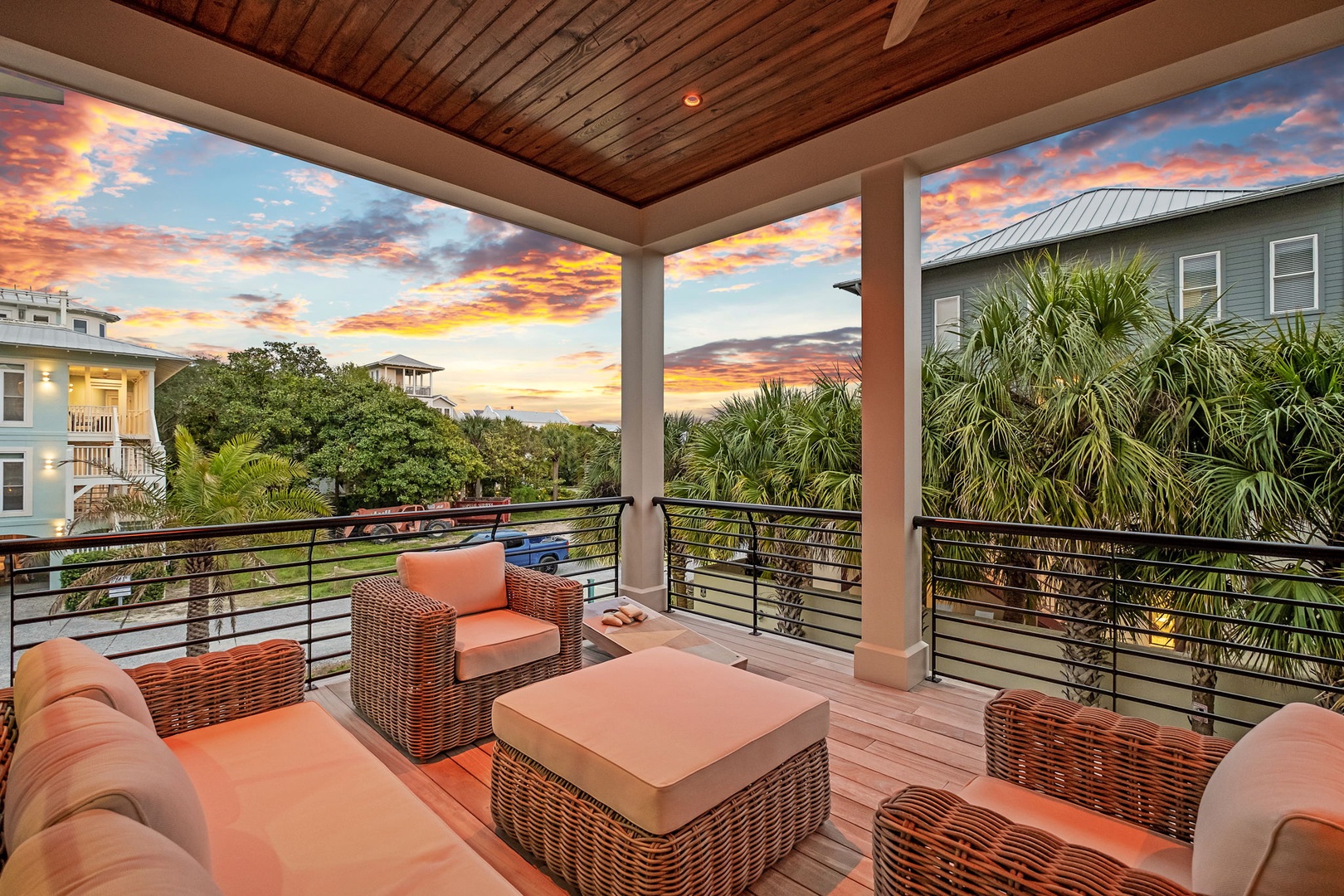 Unwind on your private covered terrace with plush wicker seating as vibrant sunset colors paint the sky above tropical palms.