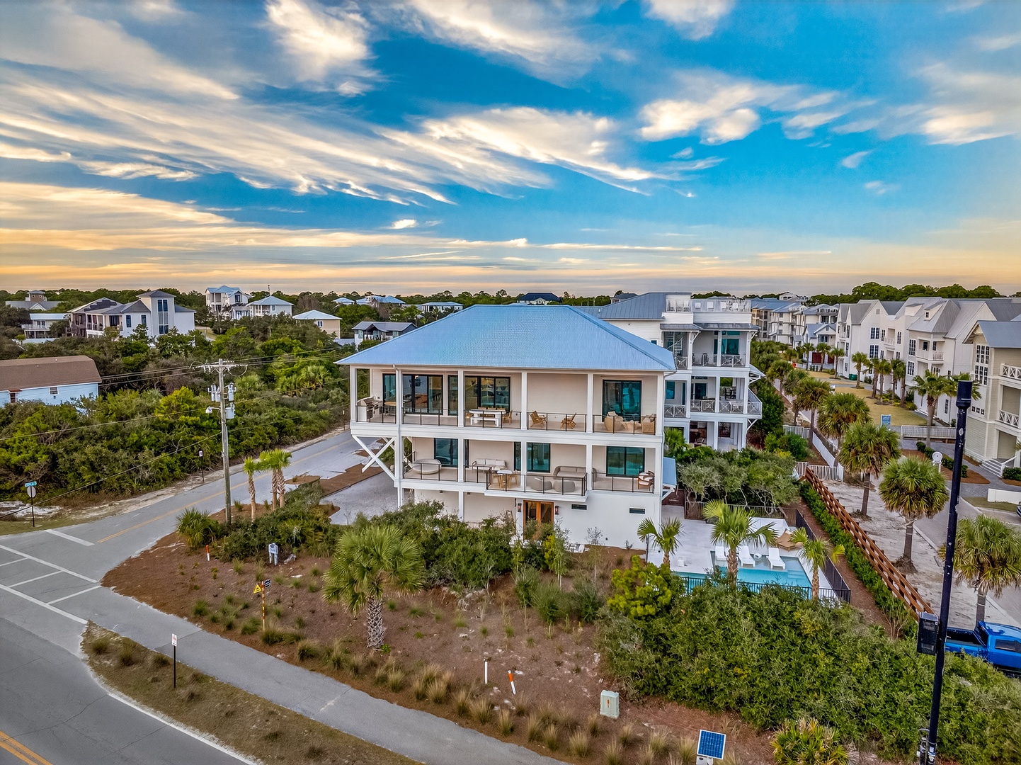 Elevated beach house featuring multiple covered porches and private pool, nestled among coastal palms in a quiet residential neighborhood.