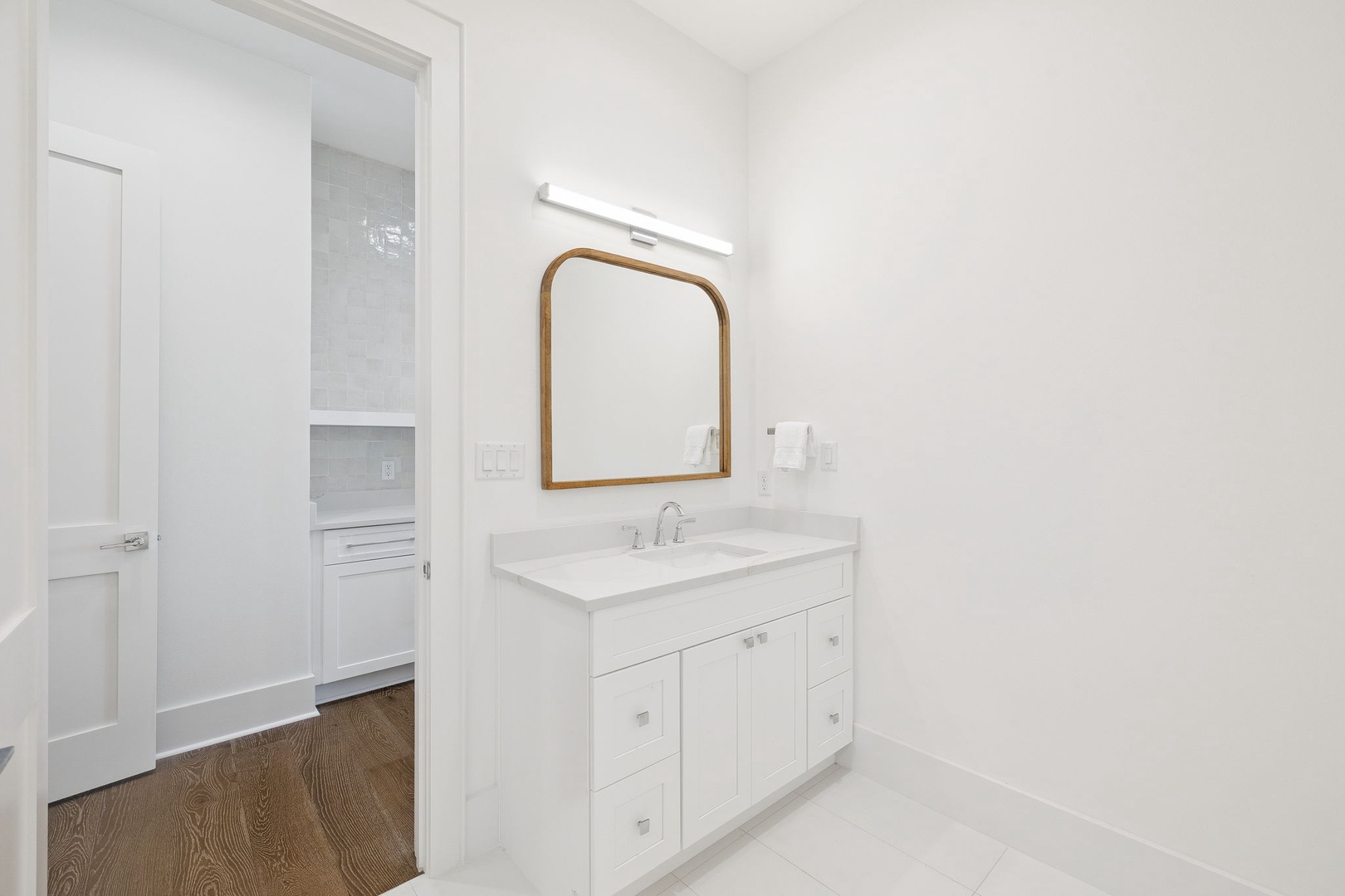 Step into your pristine ensuite with gleaming white vanity, warm wood-framed mirror, and modern lighting creating a spa-like sanctuary.